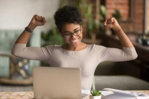 find your dream job young black woman in front of computer with hands raised in victory